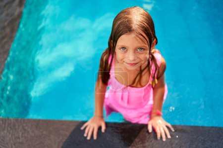 Child smiles, plays in water, leisure activity. Happy girl in pink swimsuit enjoys summer day in kids pool at resort. Outdoor family vacation, tropical climate, fun swimming, childhood joy.