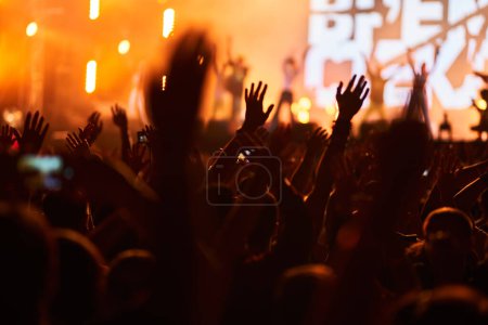 Konzertbesucher genießen die Live-Performance und die lebendige Festivalatmosphäre. Aufgeregtes Publikum beim Open-Air-Musikfest, Hände hoch jubelnd unter Bühnenbeleuchtung, Abendveranstaltung. Energetische Party-Stimmung, Fans feiern.