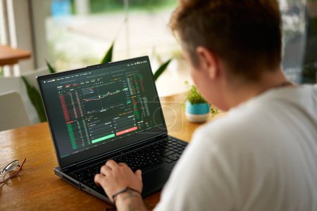 Person trades digital currency, researches investment amid tech savvy peers. Focused crypto trader analyzes market trends on laptop at coworking space, blockchain analytics visible on screen.