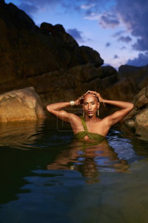 Photo for Androgynous black lgbtq fashion model dives out of the water inside a picturesque natural pool. Non-binary biethnic person poses waist deep in still water among rocks on exotic island. Pride month. - Royalty Free Image