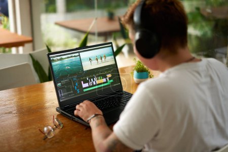 Editing beach scene timeline, focus on creative process in home office. Professional video editor works on laptop with editing software, headphones on. Casual work environment, multimedia project.
