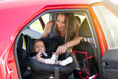 Junge Mutter setzt ihren kleinen Sohn in den Autositz und schnallt sich an