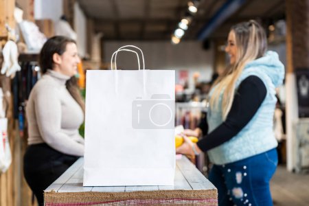Bolsa blanca con espacio para texto en un mostrador de tienda de ropa con una vendedora y un cliente en una tienda de ropa de talla grande.