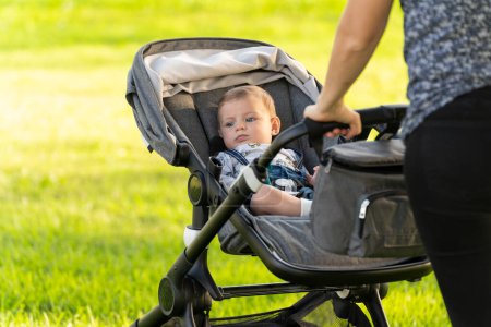 Foto de Madre e hijo caminando con el cochecito del bebé en el parque sobre la hierba verde - Imagen libre de derechos