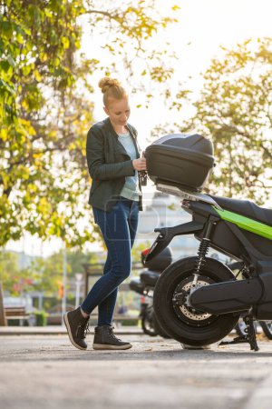 Foto de Retrato vertical de mujer pelirroja abriendo el maletero de su motocicleta aparcada - Imagen libre de derechos
