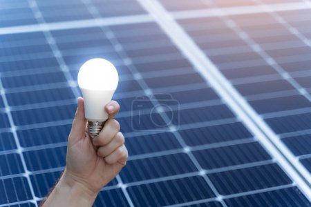 Photo for Image with copy space of energy saving concept with solar panels and a hand holding a light bulb - Royalty Free Image