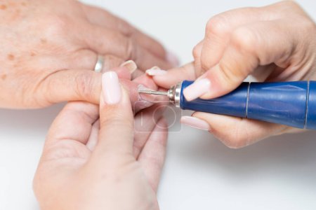 Close-up of a real female manicurist scraping a senior womans fingernail cuticle with a nail buffer