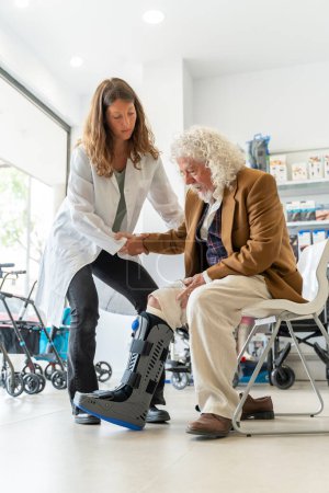 Älterer Mann mit lockigem weißen Haar probiert in der Apotheke einen orthopädischen Stiefel an