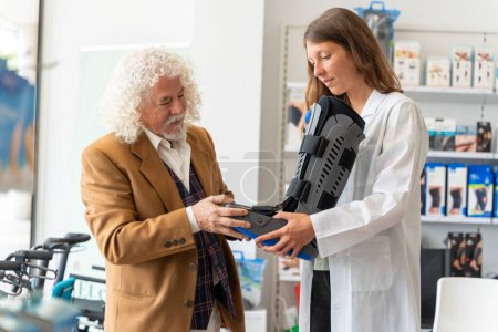 Senior man with curly white hair tries on an orthopedic boot at the pharmacy