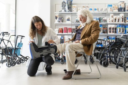 Älterer Mann mit lockigem weißen Haar probiert in der Apotheke einen orthopädischen Stiefel an