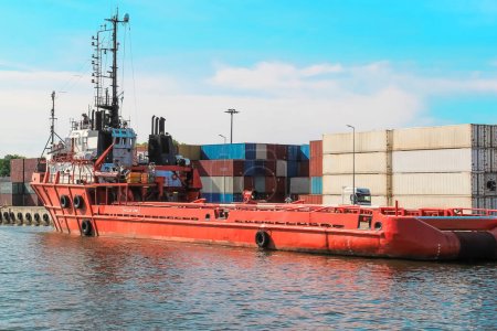 Una ajetreada escena del puerto con un buque de carga rojo atracado en el muelle, rodeado de grúas, edificios industriales y otros buques de carga. La atmósfera vibrante del transporte marítimo y la logística en acción.