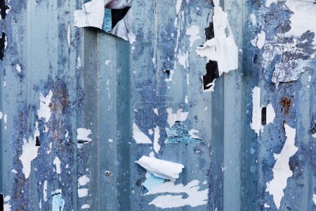 Un mur en métal ondulé bleu altéré avec de la peinture pelante et du papier déchiré, révélant une surface en détresse sous. Le contexte industriel ajoute de la texture aux projets de design.