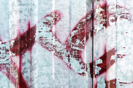 Téléchargez les photos : This textured metal sheet features a striking contrast between the silver surface and the bold red graffiti, giving it a weathered and industrial look with a touch of artistic flair. - en image libre de droit