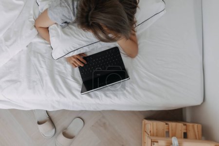 Foto de Mujer asiática dormir en el ordenador tableta en la cama por la mañana. Trabajo en línea temprano. - Imagen libre de derechos