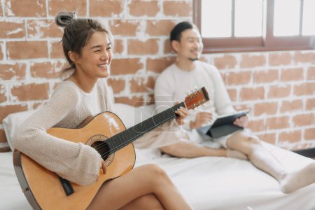 Asian woman play guitar for man in happy warm day off. Concept of hobby activity