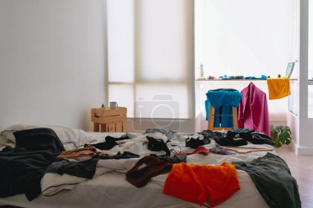Téléchargez les photos : Chambre à coucher d'appartement encombrée et désordonnée pleine de vêtements colorés partout. - en image libre de droit