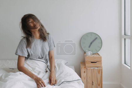 Photo for Asian woman just wake up by the clock at 7 AM on the bed in the morning. - Royalty Free Image