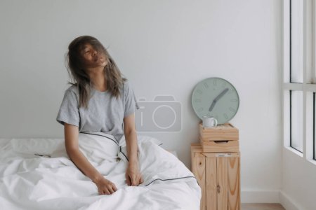 Photo for Asian woman just wake up by the clock at 7 AM on the bed in the morning. - Royalty Free Image