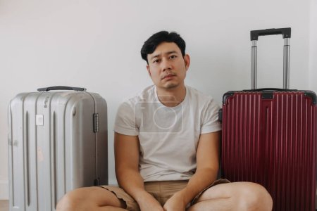 Sad disappointed asian man sit with his luggages as his traveling trip plan has been cancelled.