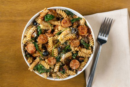 Téléchargez les photos : Pâtes rotini servies avec des saucisses italiennes et des épinards sautés. - en image libre de droit