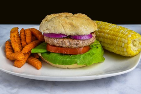 Photo for Turkey burger top  with red onions  and served with corn on the cob  and fries. - Royalty Free Image