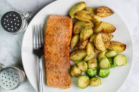 Photo for Seasoned baked salmon served with potato wedges and roasted brussel sprouts - Royalty Free Image