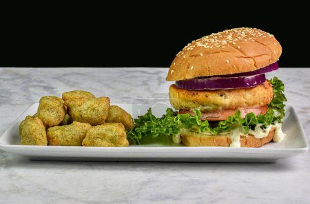 salmon burger with with onion lettuce and tarter sauce  served with veggie tots.