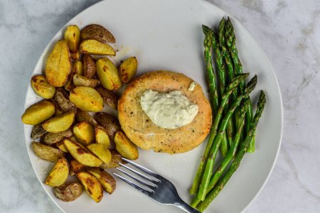 salmon burger  top with  tarter sauce served with sauteed asparagus and potato wedges,