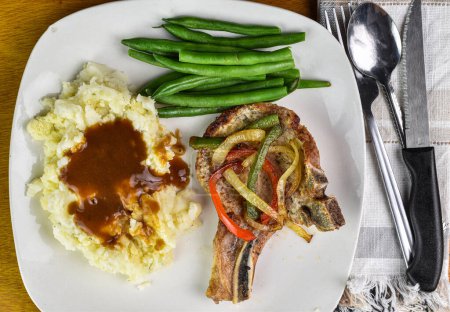 pork chop top with onions and peppers  served with masn potatoes , gravy and green beeans