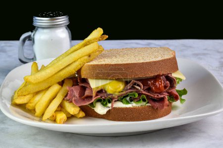 pastrami sandwich top with swiss cheese  on wheat bread served with fries, 