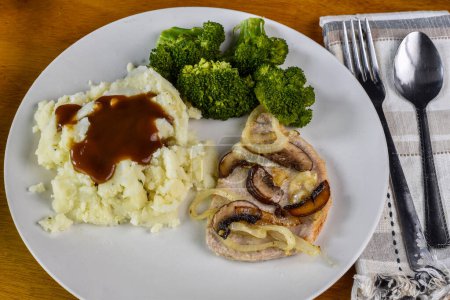  baked pork chop top with oniond and mushrooms served  with broccoli and mashed potatoes