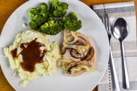 thin baked pork chop top with oniond and mushrooms served  with broccoli and mashed potatoes