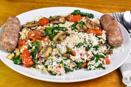 Foto de Tapa de arroz blanco con espinacas salteadas, tomates y champiñones servidos con salchichas italianas, - Imagen libre de derechos