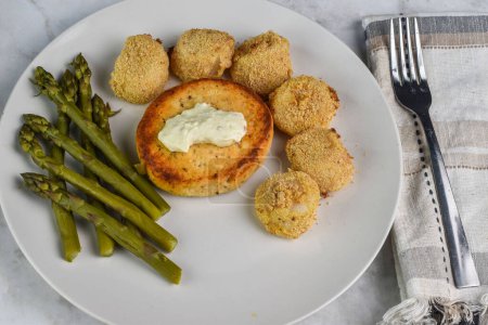 salmon burger top with tarter sauce served with baked scallops and asparagus