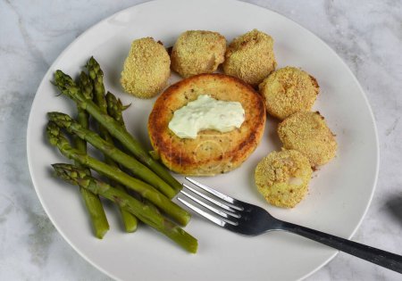 salmon burger top with tarter sauce served with  asparagus and baked scallops