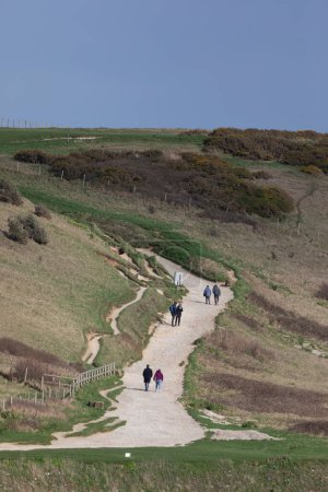 Foto de West Lulworth, Dorset, Inglaterra, Reino Unido - 1 de marzo de 2024: Personas caminando por el camino erosionado cerca de Durdle Door a la luz del sol al final de la tarde - Imagen libre de derechos