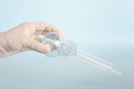 Lampenspritze, Bewässerungsstaubsauger. Chirurgische Instrumente, isoliert auf hellblauem Hintergrund, von der Hand des Arztes mit weißen Handschuhen gehalten. Geschlossener Winkel. Kopierraum. Echte Menschen. 