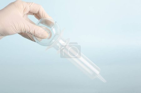 Bulb syringe, irrigation vacuum cleaner. Surgical instruments, isolated on light blue background, held by doctor's hand with white gloves. Closed angle. Copy space. Real people. 