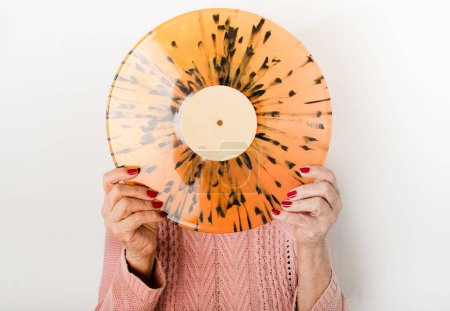 Senior woman with vinyl record facing forward covering her face. Close upe. Retro music. Long play. LP.
