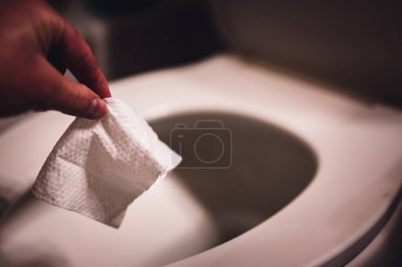 Téléchargez les photos : Les lingettes jetables étant jetées dans une toilette où elles peuvent causer un colmatage et des problèmes avec le traitement des eaux usées. Photo de haute qualité - en image libre de droit