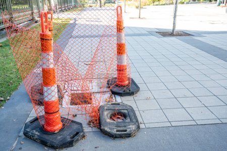 Open cover on a sidewalk access panel with hazard cones and fencing. High quality photo