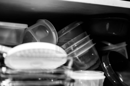 Narrow depth of field picture of an open kitchen cabinet with an assortment of containers and mismatched lids stacked. High quality photo
