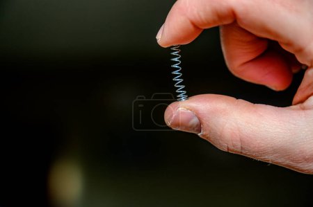 Foto de Mano caucásica comprimiendo un resorte metálico entre el pulgar y el dedo. Foto de alta calidad - Imagen libre de derechos