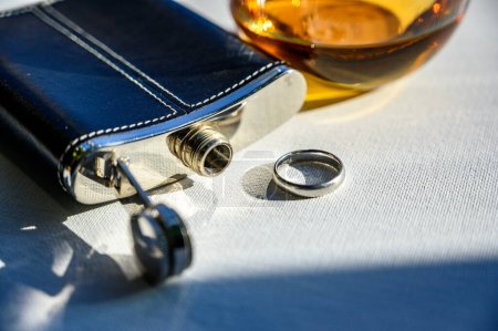 Téléchargez les photos : Flacon de whisky noir et argent à côté d'un verre de liquide ambré et d'une bague de mariage. Photo de haute qualité - en image libre de droit