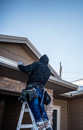 Photo for Contractor installing gutters on a residential building in the winter with snow on the roof. High quality photo - Royalty Free Image
