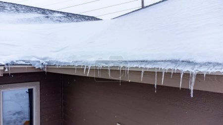 Erhöhter Blick auf einen Eisdamm und Schnee auf einem Wohnhausdach. . Hochwertiges Foto