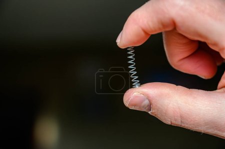 Caucasian hand compressing a metal spring between a thumb and finger. High quality photo