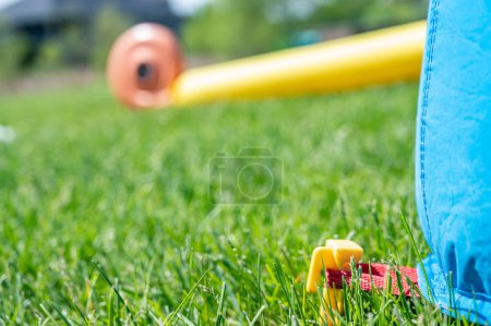 Téléchargez les photos : Focus on grass with blurred bouncy house stake pinned into turf. High quality photo - en image libre de droit