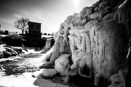 Téléchargez les photos : Cascade du parc Sioux Falls avec glace et neige. L'eau de fonte des neiges en cascade se déversant sur le dessus dans une piscine d'eau stagnante. Photo de haute qualité - en image libre de droit