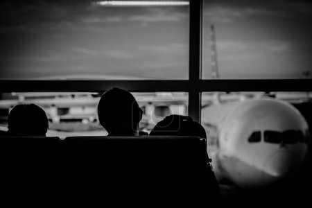 Silhouette zweier junger Erwachsener, die in einem Flughafenterminal mit einem defokussierten Flugzeug aus dem Fenster geschlurft sind. Hochwertiges Foto